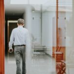 man in white dress shirt and gray denim jeans standing in front of glass window